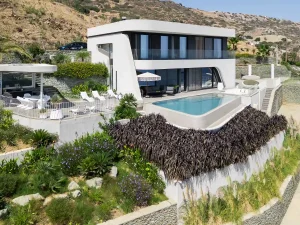 Aerial view of Meltemi Villa with infinity pool and landscaped gardens overlooking the sea.