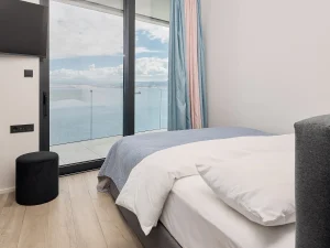 Minimalist bedroom with soft blue tones and balcony overlooking the Aegean Sea.