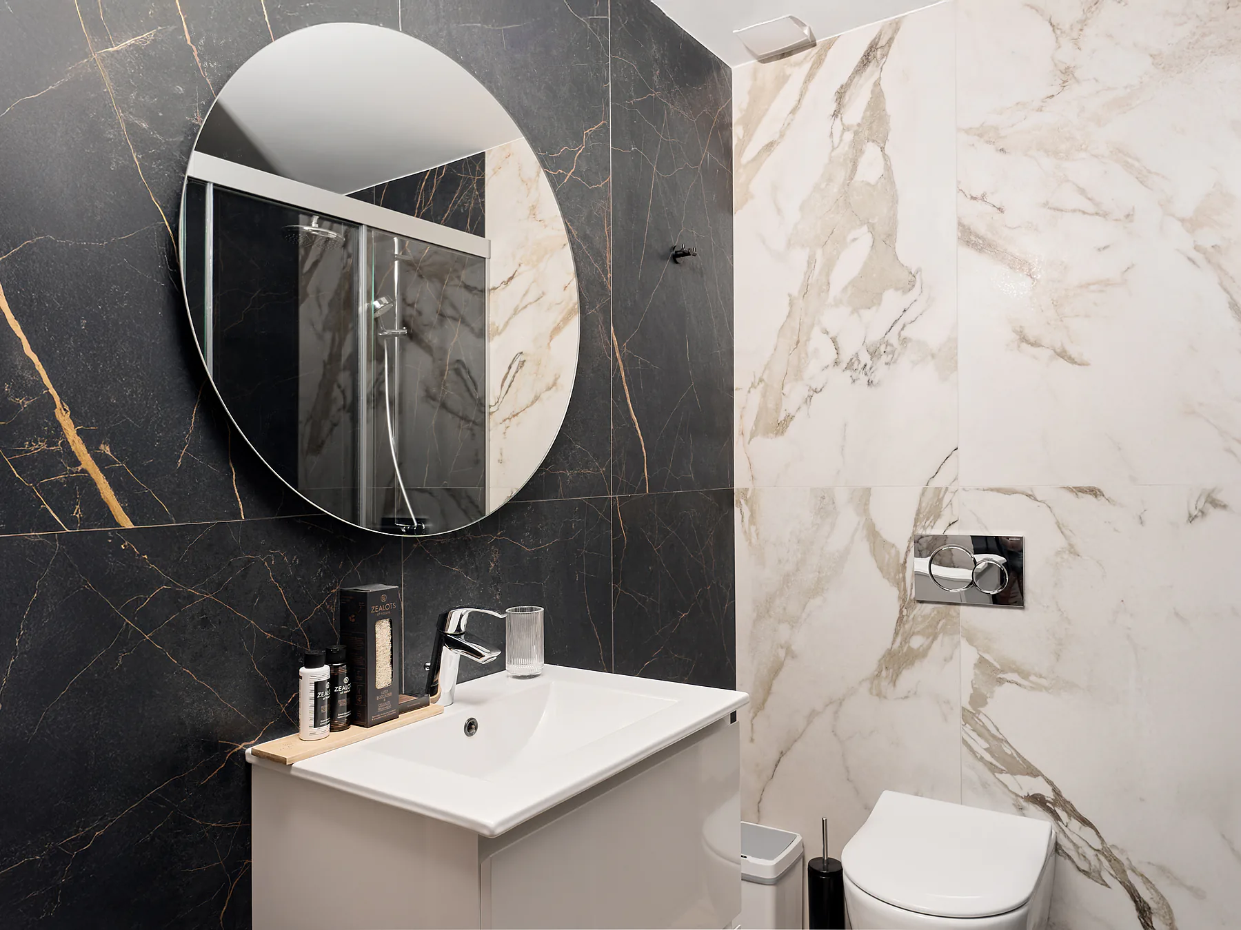 Elegant bathroom with black tiles, round mirror, and designer fixtures.