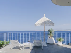 Oceanfront terrace with white loungers, umbrella, and panoramic sea view.