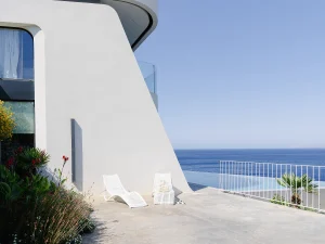 Modern villa terrace with sculpted white loungers and panoramic view of the Aegean Sea.