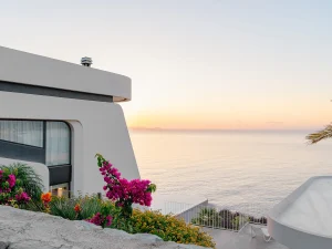 Modern villa terrace adorned with colorful flowers overlooking the calm Aegean Sea at sunset.