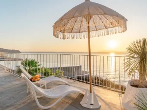 Ocean-view terrace with sun umbrella and lounge chairs overlooking the Cretan coast.