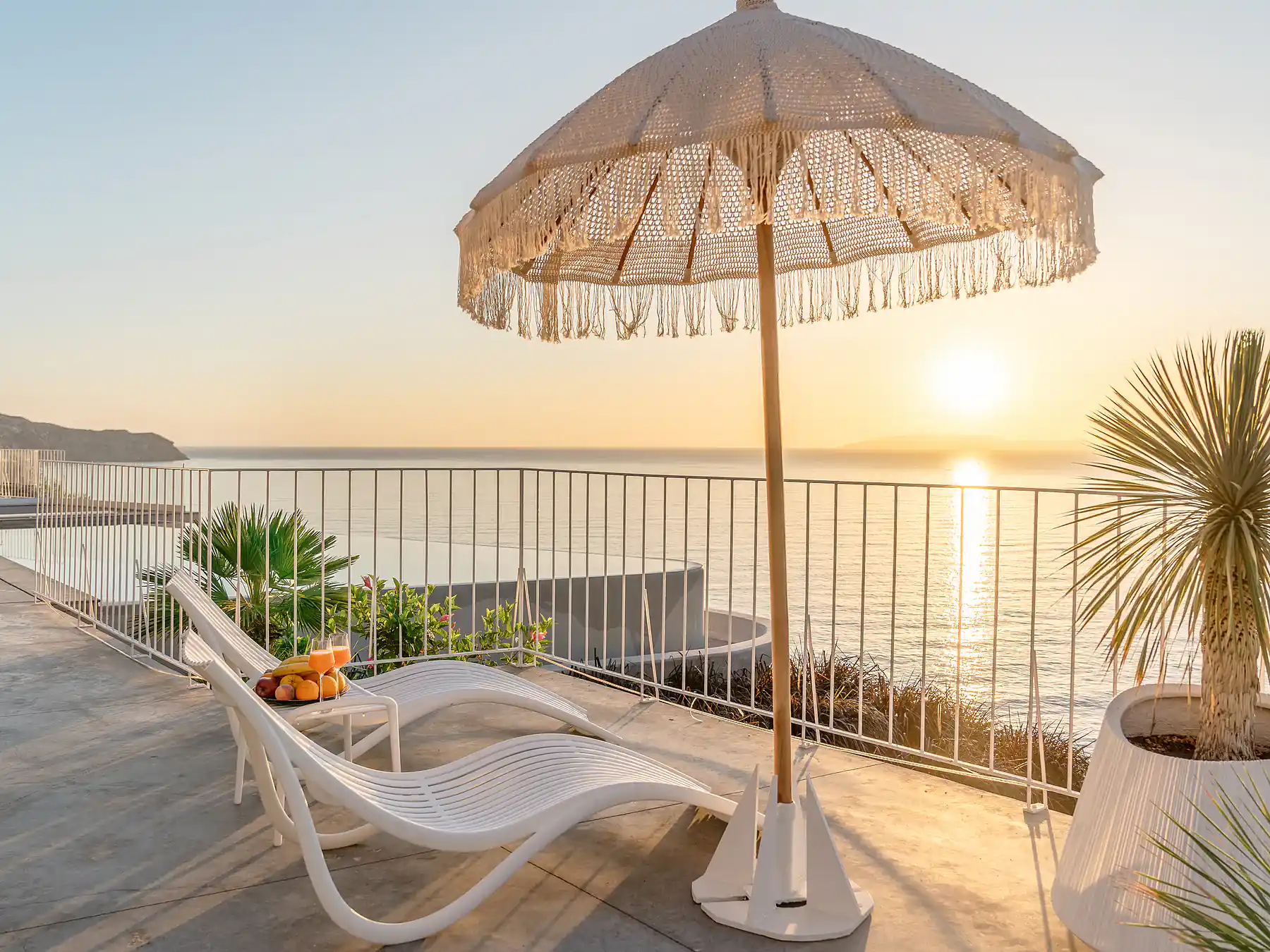 Ocean-view terrace with sun umbrella and lounge chairs overlooking the Cretan coast.